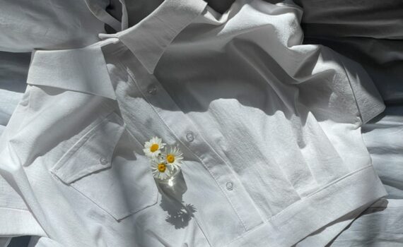 a white shirt laying on top of a bed next to a flower