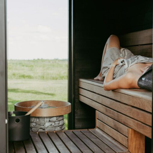 Person relaxing in a wooden sauna with outdoor view.