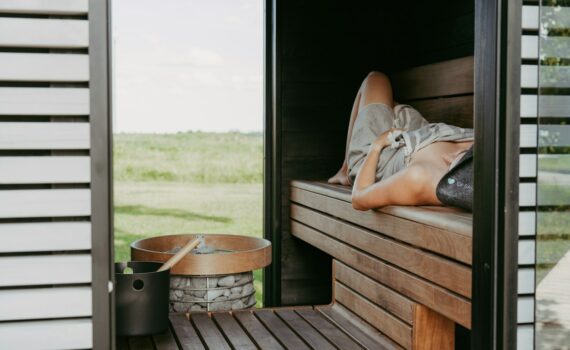 Person relaxing in a wooden sauna with outdoor view.